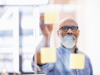 Shot of a businessman plotting out a plan with markers on a glass wall in his office