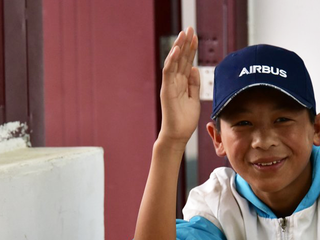 Young boy waving his hand, wearing an Airbus cap.