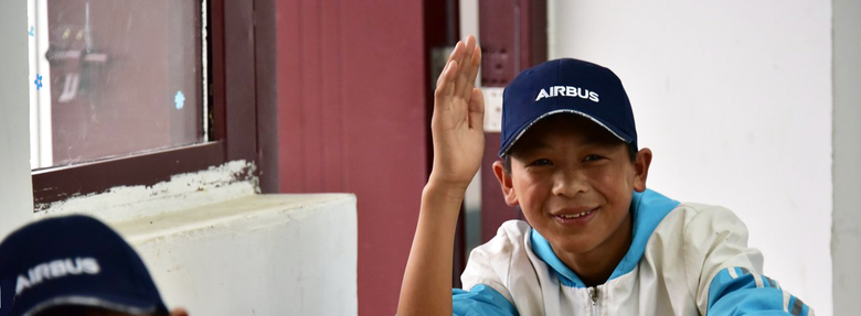 Young boy waving his hand, wearing an Airbus cap.