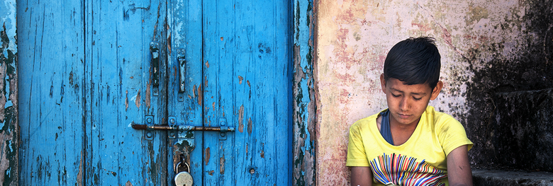 Boy sitting on steps near the door with rusty lock.