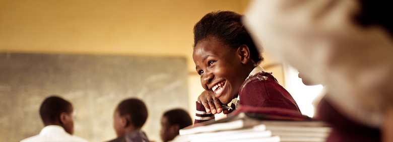 A Happy young South African girl (from the Xhosa tribe) works on her studies and jokes with her friends at at an old worn desk in a class room in the Transkei region of rural South Africa.
